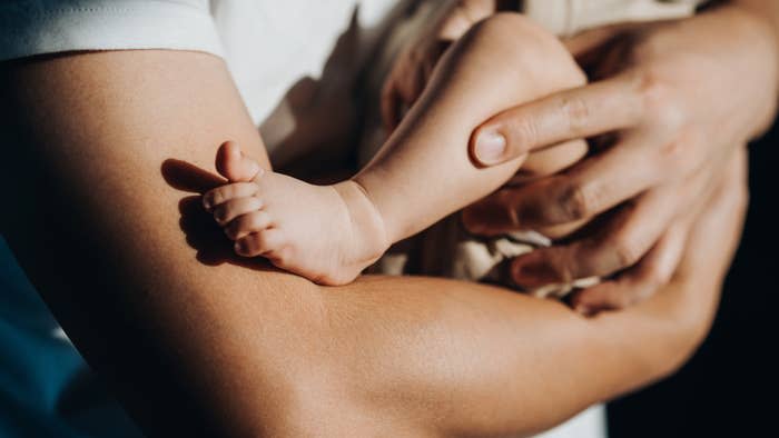 Close-up of an adult holding a baby's leg and foot tenderly in their hands, symbolizing parental care and affection