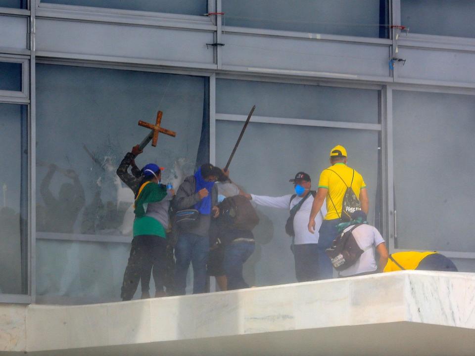 Supporters of Brazilian former President Jair Bolsonaro break a window as they invade Planalto Presidential Palace