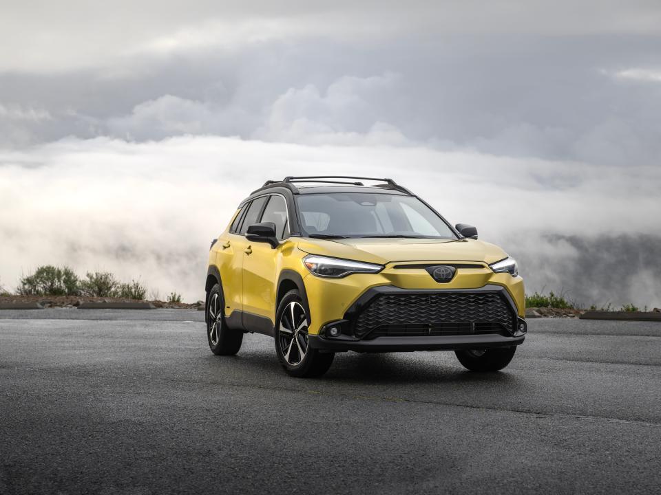 A yellow SUV is parked on dark pavement in front of a gloomy landscape.