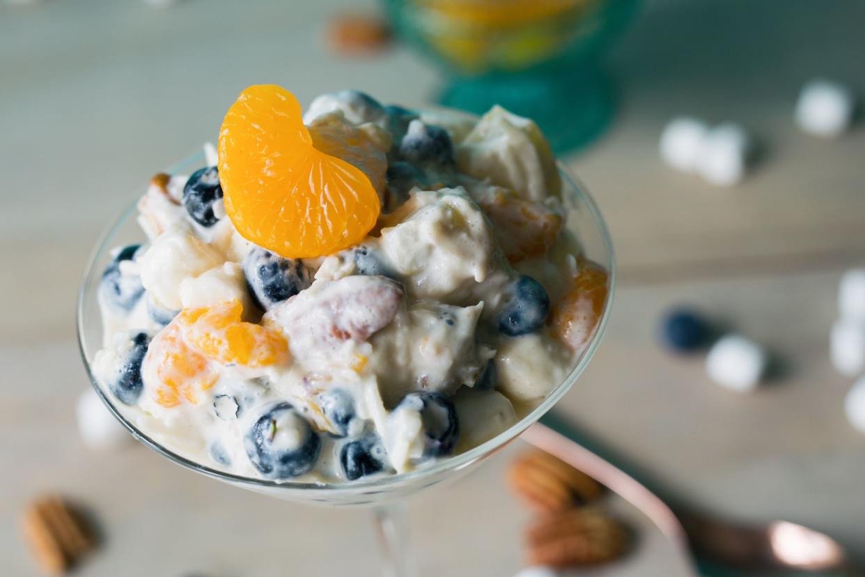 Serving of clementine ambrosia in a martini glass, spilled marshmallows and pecans in the background. Close view