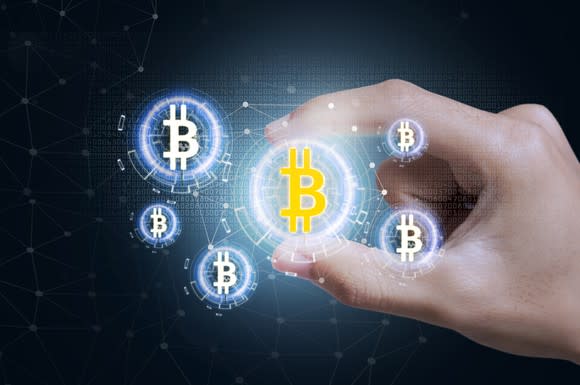 A hand holding an illustrated digital bitcoin token, representing the digital currency of the same name.