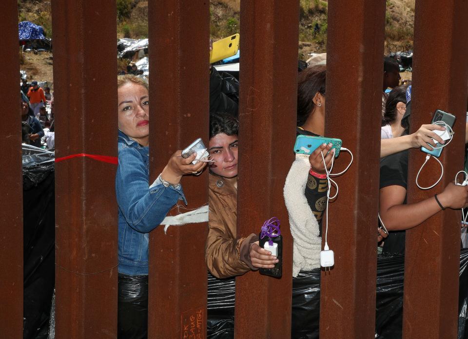 Migrants try to get help charging their phones from journalists and humanitarians working near the border fence near Monument Rd. close to the International Wastewater Treatment Plant in San Diego, Calif., May 11, 2023. 