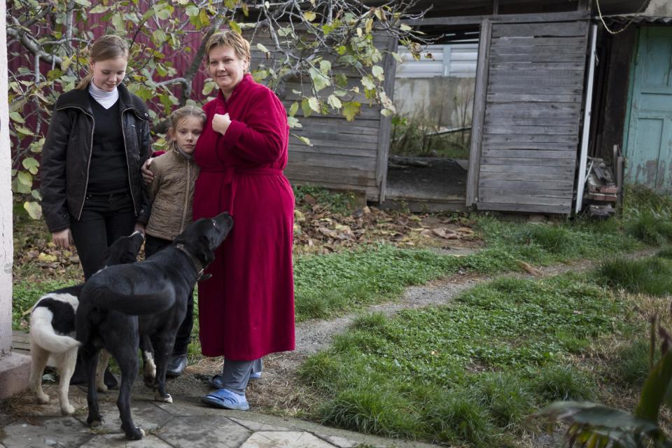 In this photo taken on Wednesday, Nov. 27, 2013, Alexandra Krivchenko, right, and her children, center, play with the dogs in the yard of a house sandwiched between the railway and a federal highway (seen in the background) in the village of Vesyoloye outside Sochi, Russia. As the Winter Games are getting closer, many Sochi residents are complaining that their living conditions only got worse and that authorities are deaf to their grievances. (AP Photo/Alexander Zemlianichenko)