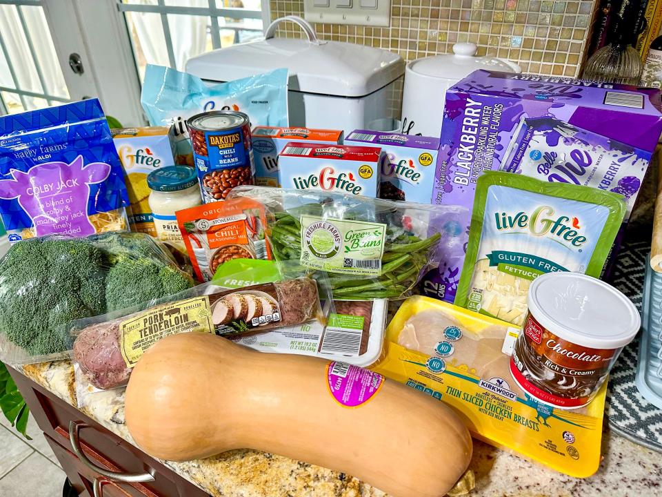 A kitchen counter with groceries from Aldi, including chocolate frosting, a butternut squash, chicken breast, pork tenderloin, broccoli, green beans, sparkling water, liveGfree products, and chili beans