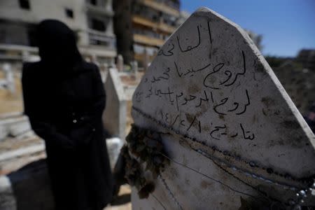 A woman stands next to a grave in a cemetery at al-Kalasa district of Aleppo July 14, 2017. REUTERS/ Omar Sanadiki