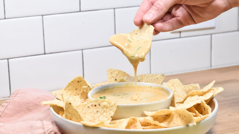 hand scooping tortilla chip into queso dip