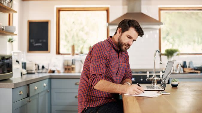 Shot of a handsome man sitting at his kitchen counter with his laptop.