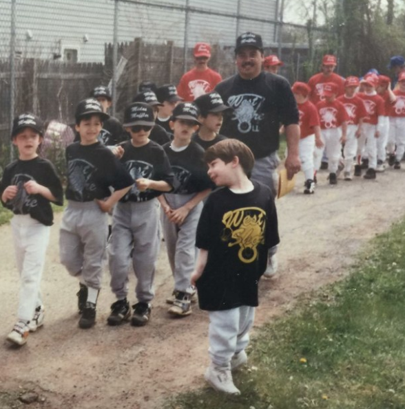 Boys on a baseball team standing next to a man and a young boy in front of them posing but not in uniform