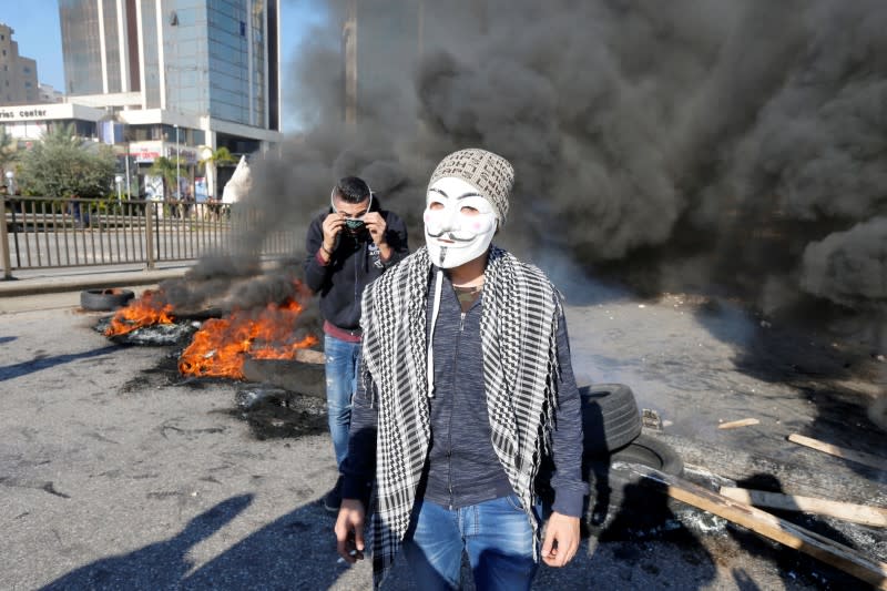 A protestor wearing an Anonymous mask walks near burning barricades during a protest over economic hardship and lack of new government in Beirut
