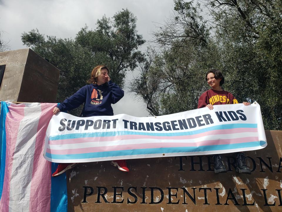 Ventura County residents Finn Samson and Sabrina Silva hold a protest sign next to a transgender pride flag at a protest against Florida Gov. Ron DeSantis outside the Ronald Reagan Presidential Library in March. Protesters are expected at the Republican presidential primary debate on Wednesday.