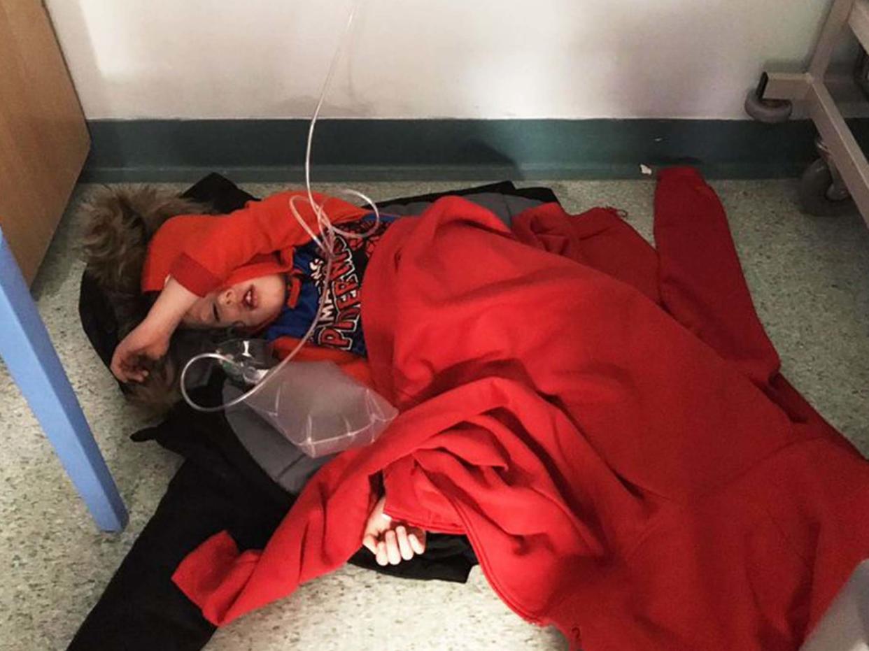 Four-year-old Jack Williment is covered in coats on the floor at Leeds General Infirmary due to a lack of beds: Mirror