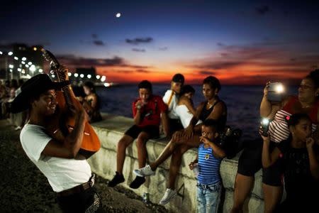 People record videos with their mobile phones of a street musician's performance during sunset at an internet hotspot along the seafront in Havana, Cuba, July 14, 2018. REUTERS/Alexandre Meneghini