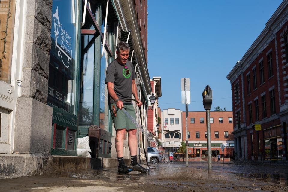 Andrew Brewer, a resident of Montpelier and former business owner on Langdon Street, helps wash away the mud from the sidewalk (Getty Images)