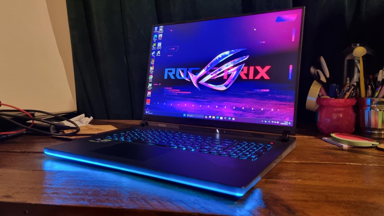  The Asus ROG Strix Scar 18 on a desk, with its RGB lights lit up in blue. 