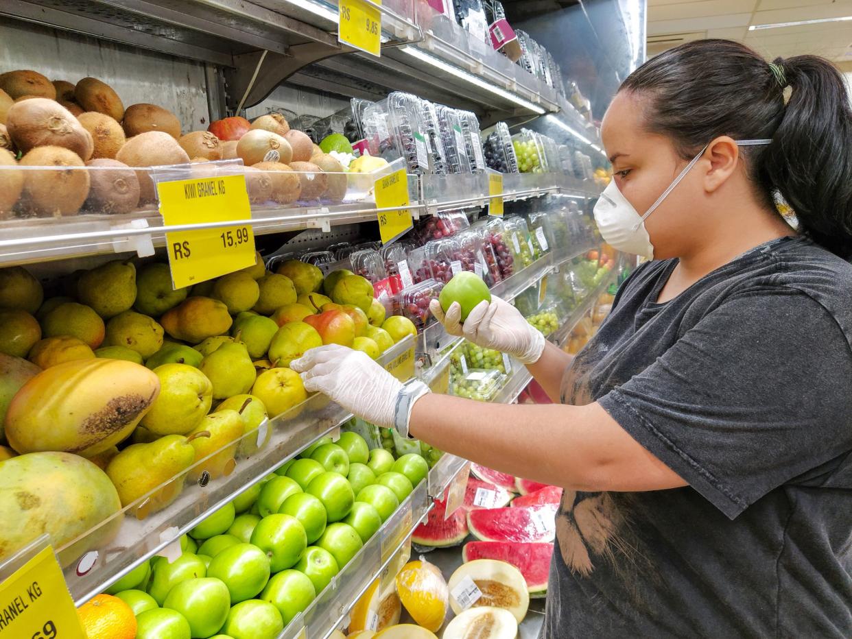 woman choosing green apples with mask and glove, protection against coronavirus in Rio de Janeiro.