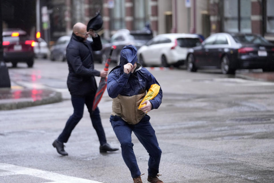 Pedestrians are buffeted by wind as they cross a street, Monday, Dec. 18, 2023, in Boston. A storm moving up the East Coast brought heavy rain and high winds to the Northeast on Monday, threatening flooding, knocking out power to hundreds of thousands. (AP Photo/Steven Senne)