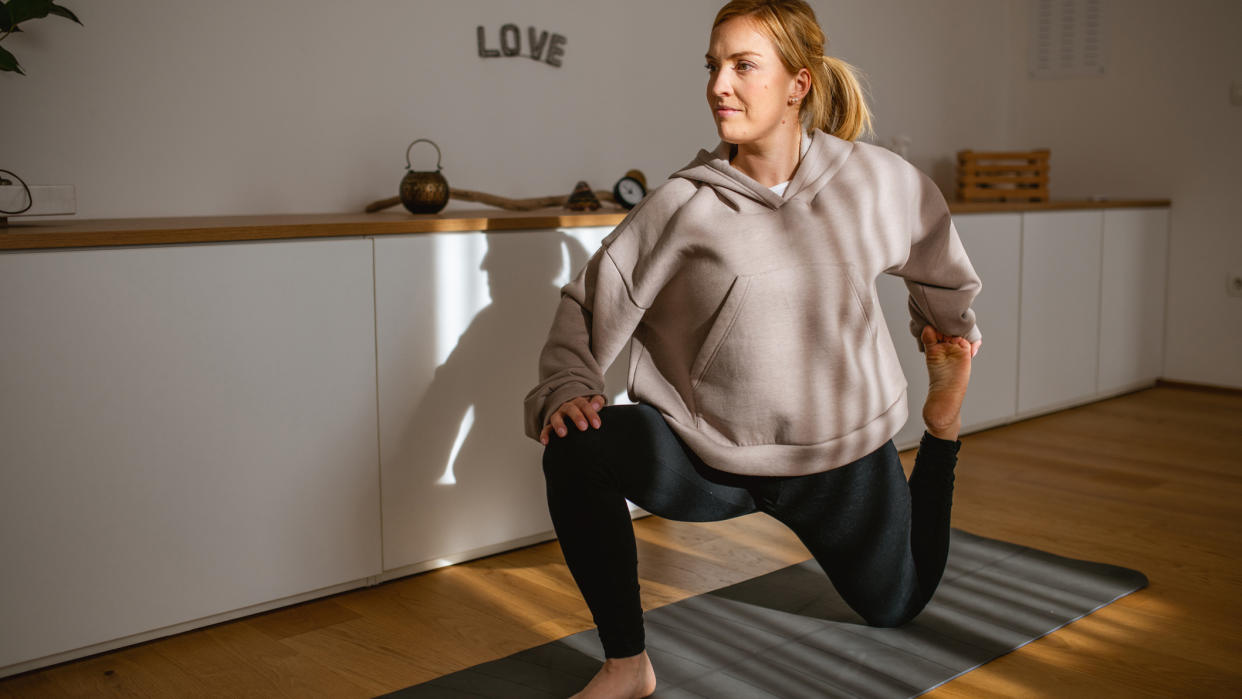  Woman doing yoga quad stretch at home. 