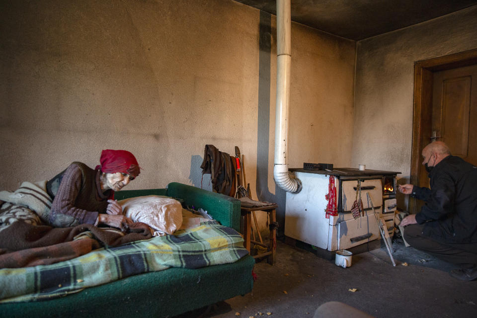 Kosovo Albanian Fadil Rama, right, lights the wooden stove for a Kosovo Serb Blagica Dicic a lonely 92-year old woman in a remote village of Vaganesh, Kosovo on Thursday, Nov. 19, 2020, abandoned by all her former ethnic Serb neighbors. Blagica Dicic is in failing health, and is the only resident of a remote ethnic Serb minority village in the mountains of eastern Kosovo that’s been abandoned by all its other inhabitants, even her own children, but Fadil Rama, 54, comes from the other side of Kosovo’s bitter ethnic divide. (AP Photo/Visar Kryeziu)