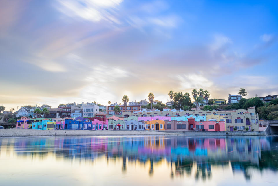 Row of brightly colored houses by water at sunset with reflection and moving clouds