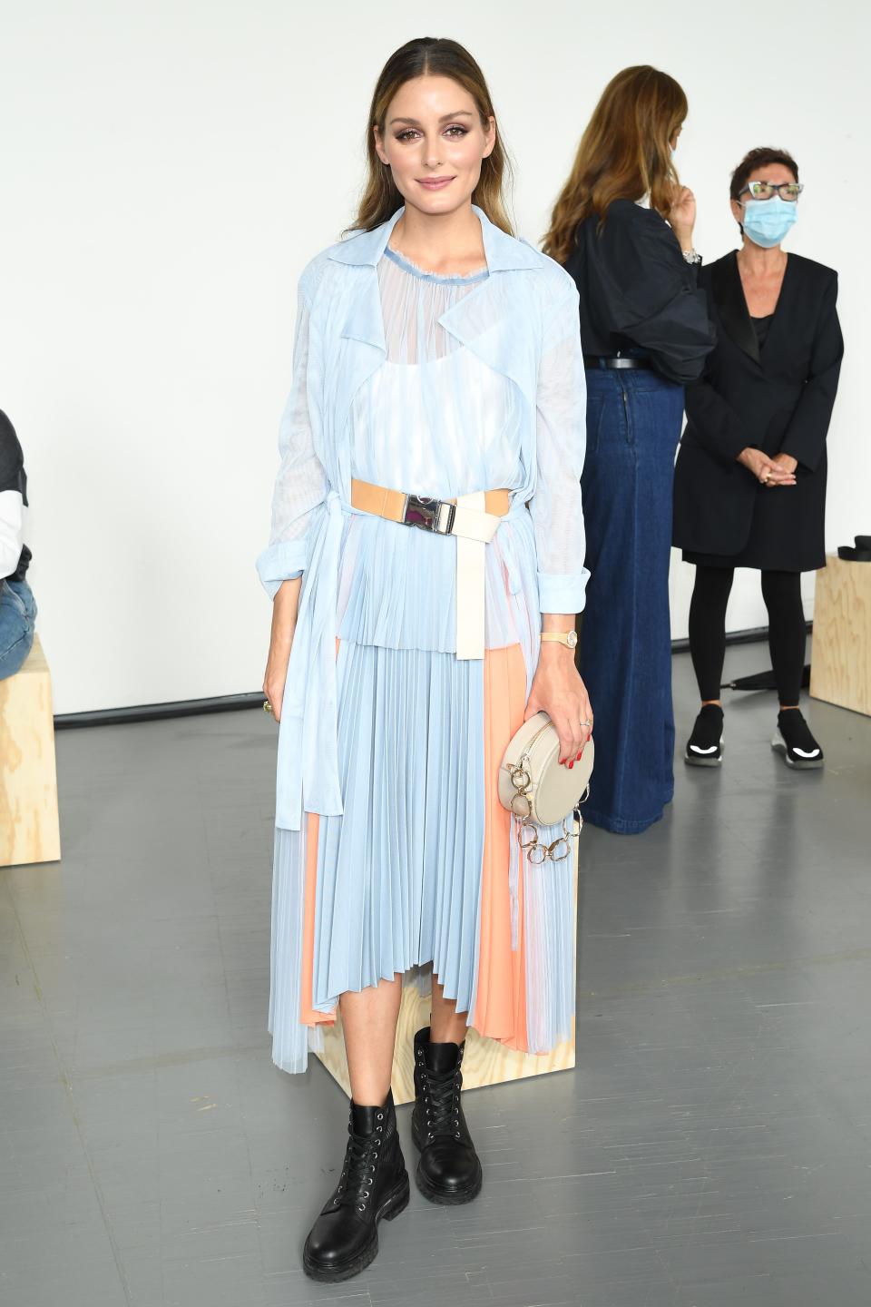 Olivia Palermo wearing a blue sheer top with a pleated skirt in a matching color with peach streaks, as well as a peach belt