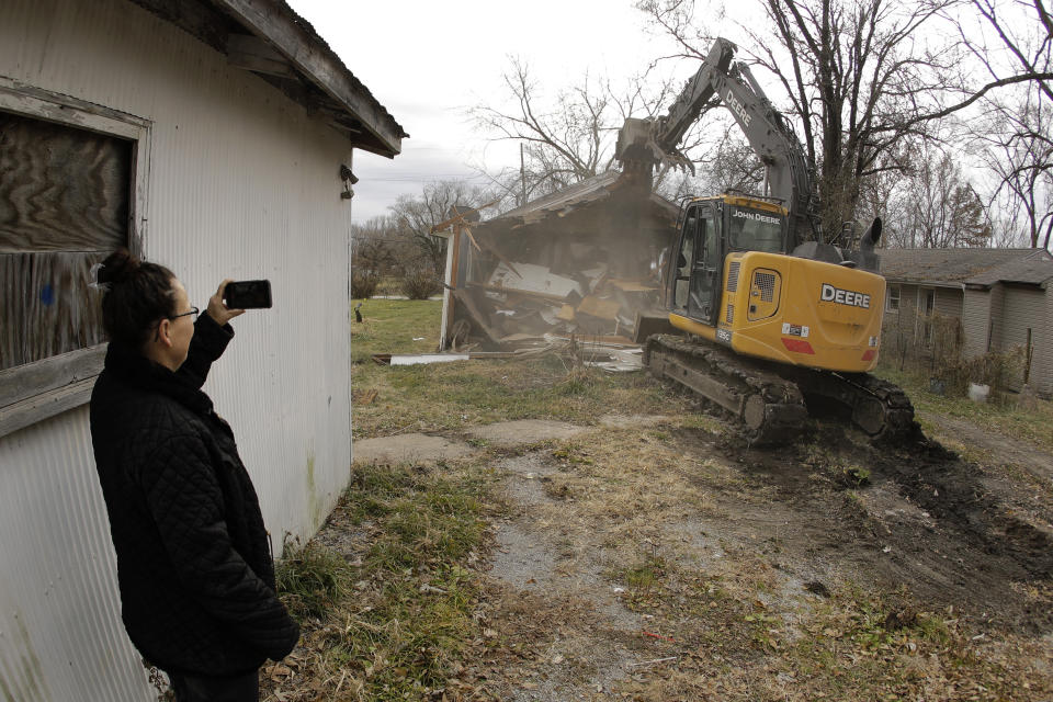 In this photo taken Monday, Nov. 18, 2019, Tammy Kilgore watches while her former home is demolished as part of a voluntary buyout in flood-prone Mosby, Mo. Kilgore accepted a $45,000 payment to leave her home of 38 years and has moved to a nearby community. (AP Photo/Charlie Riedel)