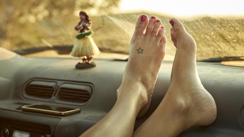 Close-up of woman's feet on dashboard. Low section of female is relaxing in mini van. She is on road trip.