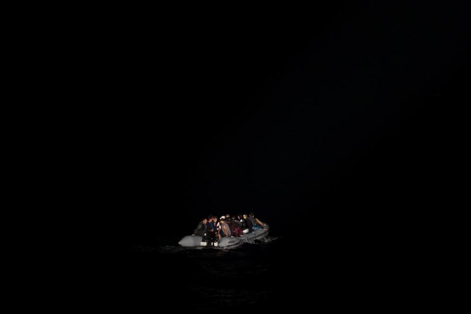 Refugees in a dinghy are lit by a a Greek coast guard patrol boat's spotlight during a rescue operation in 2019 (AP)