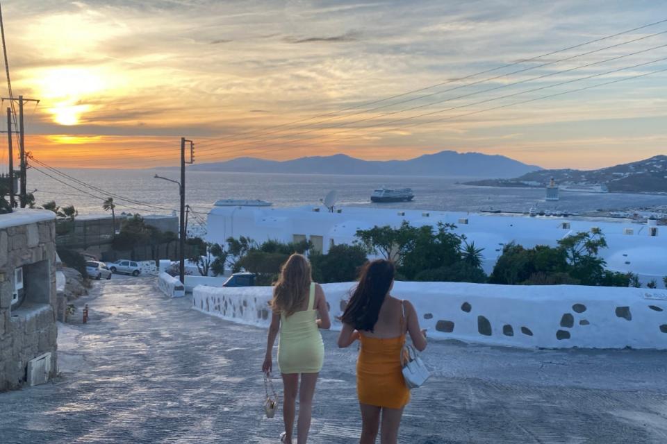 two woman walking down a hill in greece at sunset