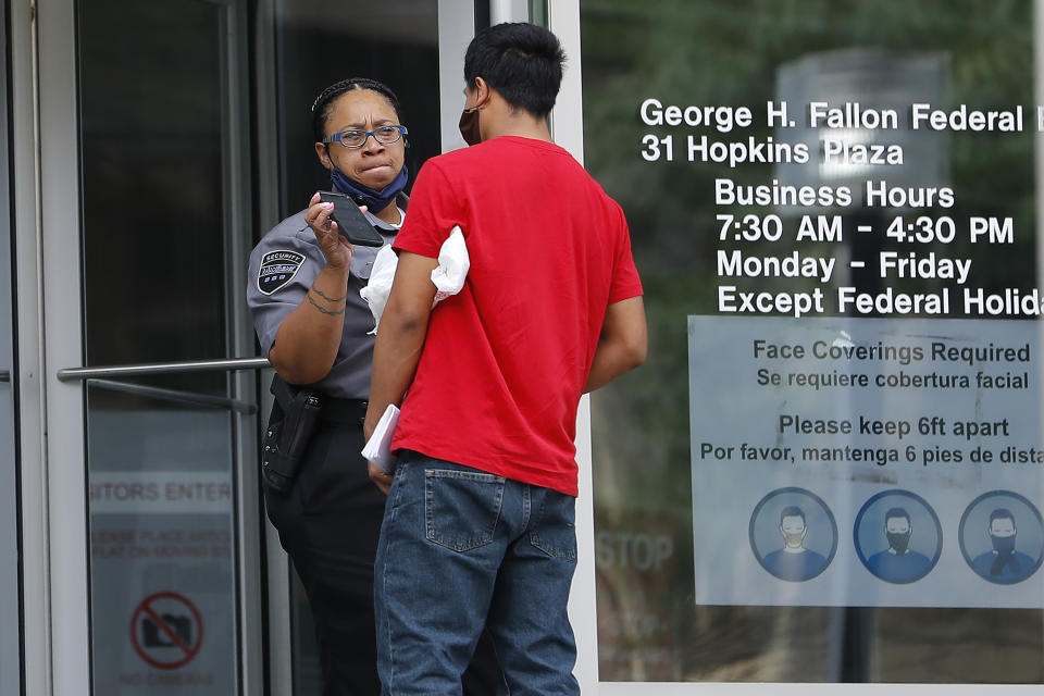 A security officer, left, shows a cell phone to a man outside the federal building, Monday, July 13, 2020, in Baltimore. Some immigration courts across the country have reopened after closing because of the coronavirus pandemic. (AP Photo/Julio Cortez)