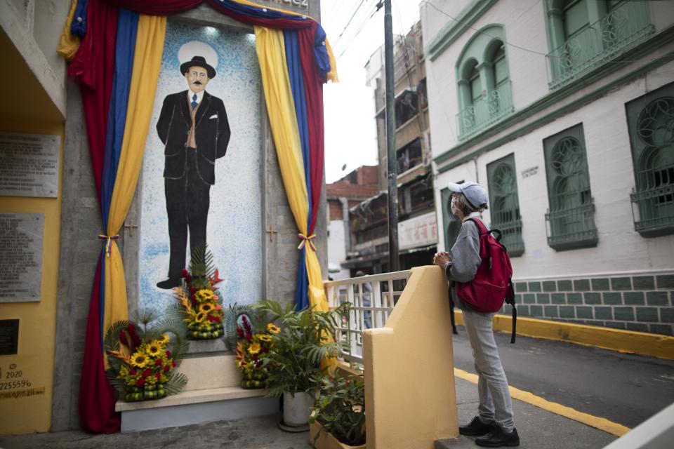 A woman prays close to a painting of Venezuelan popular saint, Dr. Jose Gregorio Hernandez at the street where he died in a car accident in 1919, in La Pastora neighborhood of Caracas, Venezuela, Wednesday, April 28, 2021. Known as the "doctor of the poor, Hernandez is set to be beatified by the Catholic church, a step towards sainthood, on April 30th. (AP Photo/Ariana Cubillos)