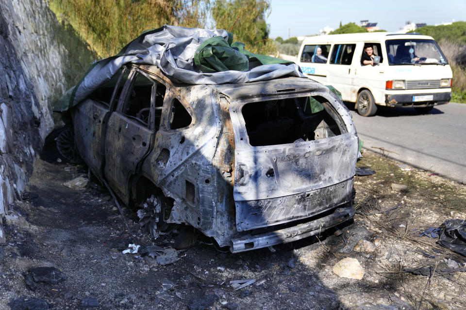 A minibus passes the attacked car that was used by the senior Hezbollah commander Wissam Tawil, who was killed on Monday, in Kherbet Selem village, south Lebanon, Tuesday, Jan. 9, 2024. An Israeli airstrike killed Tawil, who is an elite Hezbollah commander in southern Lebanon, the latest in an escalating exchange of strikes along the border that have raised fears of another Mideast war even as the fighting in Gaza exacts a mounting toll on civilians. (AP Photo/Hussein Malla)