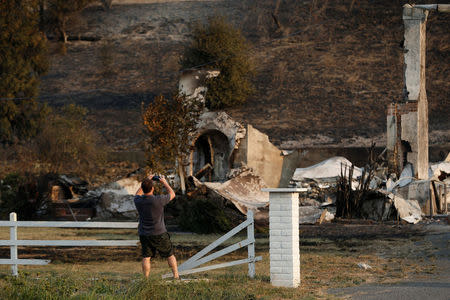 A man takes a photograph of structures destroyed by the Nuns Fire along Highway 121 in Sonoma, California, U.S., October 9, 2017. REUTERS/Stephen Lam