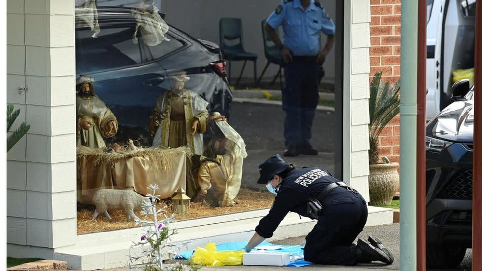 A police officer is seen on her knees carrying out forensic work outside a window displaying a life-seized nativity scene at the Assyrian Church of the Good Shepherd in Sydney (16 April 2024)