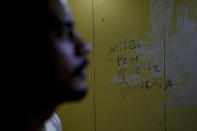 A message on a wall reads in Spanish: "Milei, worse than the pandemic" at the residential building of Ariel Heredia, front, who identifies as non-binary, as he takes the elevator to leave home in Buenos Aires, Argentina, Monday, April 15, 2024. After being fired from the dismantled Women's Ministry as part of President Javier Milei's austerity program, Heredia lost the health insurance needed to access anti-HIV medication. (AP Photo/Natacha Pisarenko)