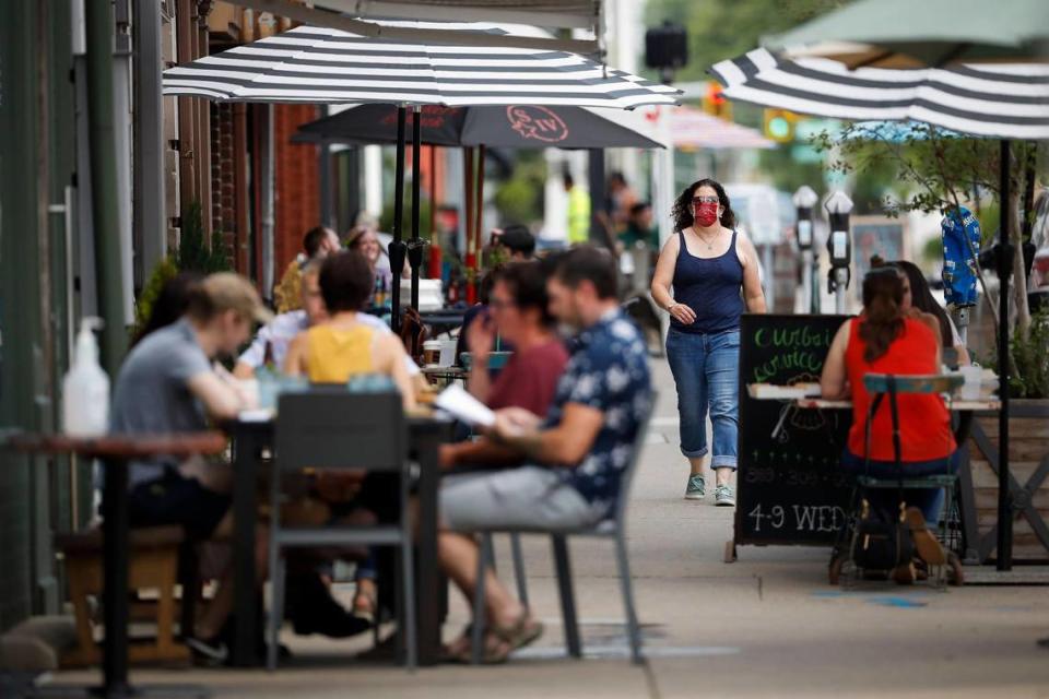 A woman wearing a mask to protect from COVID-19 walks past people eating and drinking at restaurants along North Limestone in Lexington.