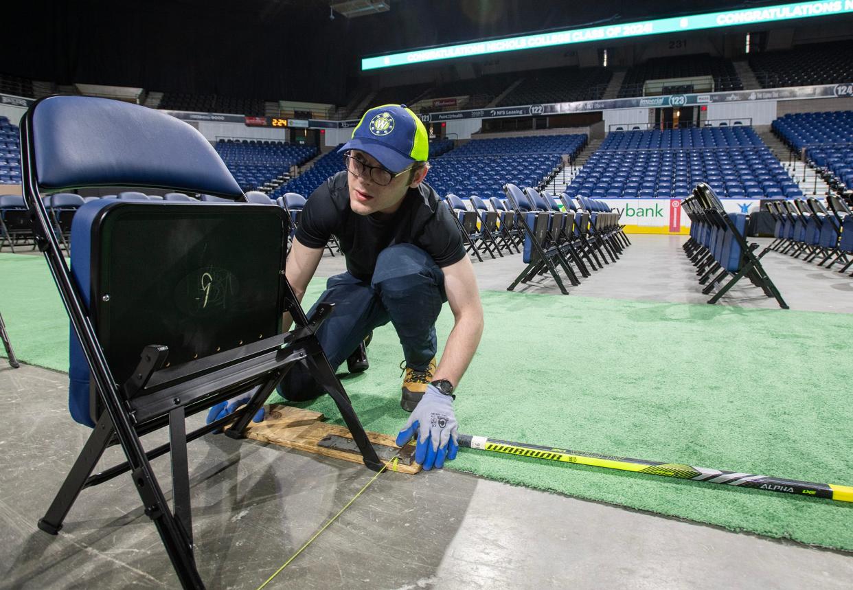 DCU Center worker Adam Brendese looks down a row of chairs as workers set up almost 400 seats on the floor of the arena Friday for the first of many graduations over the coming weeks.