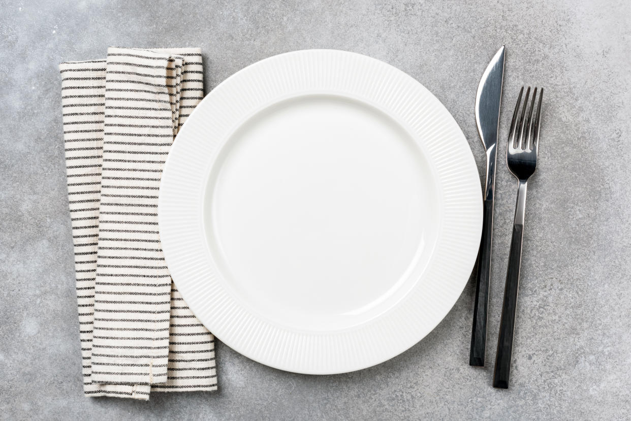 Table setting for dinner: empty plate, linen cloth and silverware. Top view, copy space