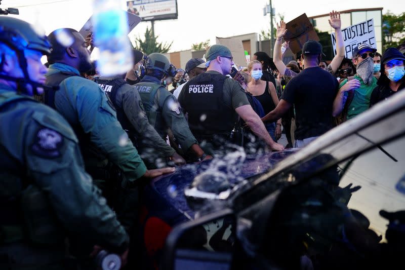 Police officers escort a police SUV from a crowd of protesters while bottles of water are thrown at them during a rally against racial inequality and the police shooting death of Rayshard Brooks, in Atlanta