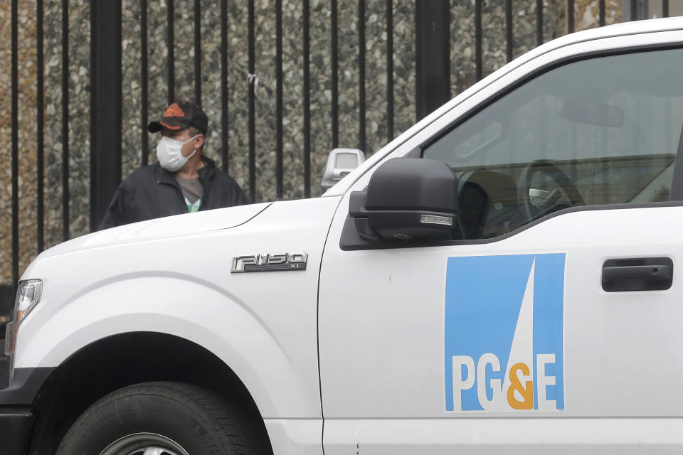 FILE - In this April 16, 2020, file photo, a man wearing a mask walks behind a Pacific Gas and Electric truck in San Francisco. Pacific Gas & Electric's proposal to pay $25.5 billion for a series of deadly Northern California wildfires ignited by its equipment faces a last-ditch effort to persuade a judge to reject the plan to get the nation's largest utility out of bankruptcy. (AP Photo/Jeff Chiu, File)