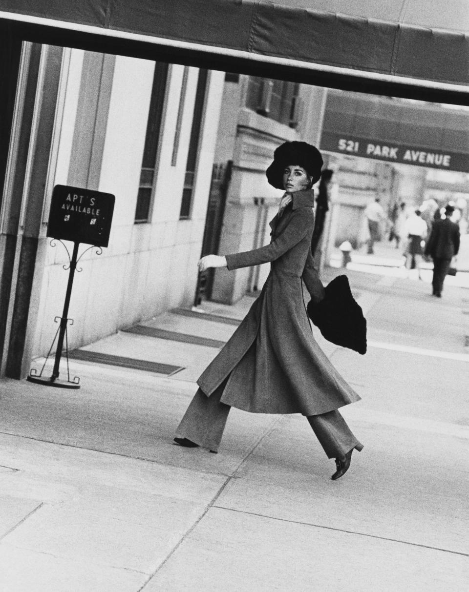 Model Windsor Elliott entering a Park Avenue apartment house, wearing a dove-gray buckskin greatcoat with high collar, fitted at the waist and flaring at the hemline, from Casa Cuero; flared-leg trousers; muskrat muff and hat from Harold Rubin. (Photo by Jack Robinson/Condé Nast via Getty Images)