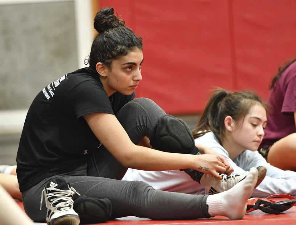 Jody Mikhail, left, unties her wrestling shoes while listening to coach Ryan Seagraves at the end of a Cumberland Valley High School team practice Tuesday, Feb. 27, 2024, in Mechanicsburg, Pa. Mikhail, a senior, began wrestling three years ago when she saw a poster in school for the girls' wrestling club. (AP Photo/Marc Levy)