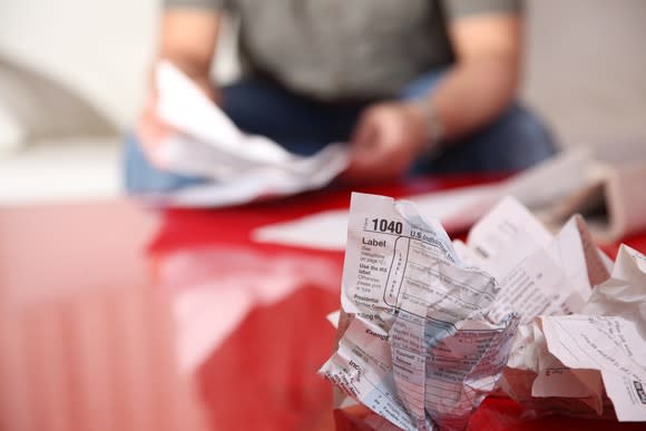 IRS tax form 1040 crumpled up on a table, with a man preparing his taxes in the background.