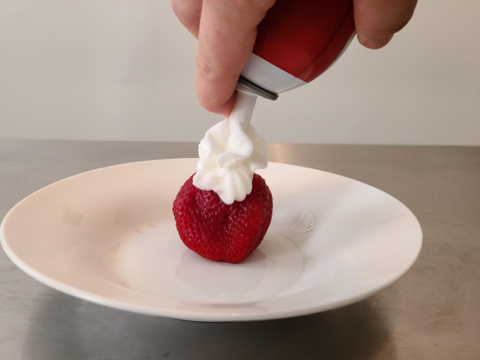 hand spraying can of reddi wip whipped cream onto a strawberry