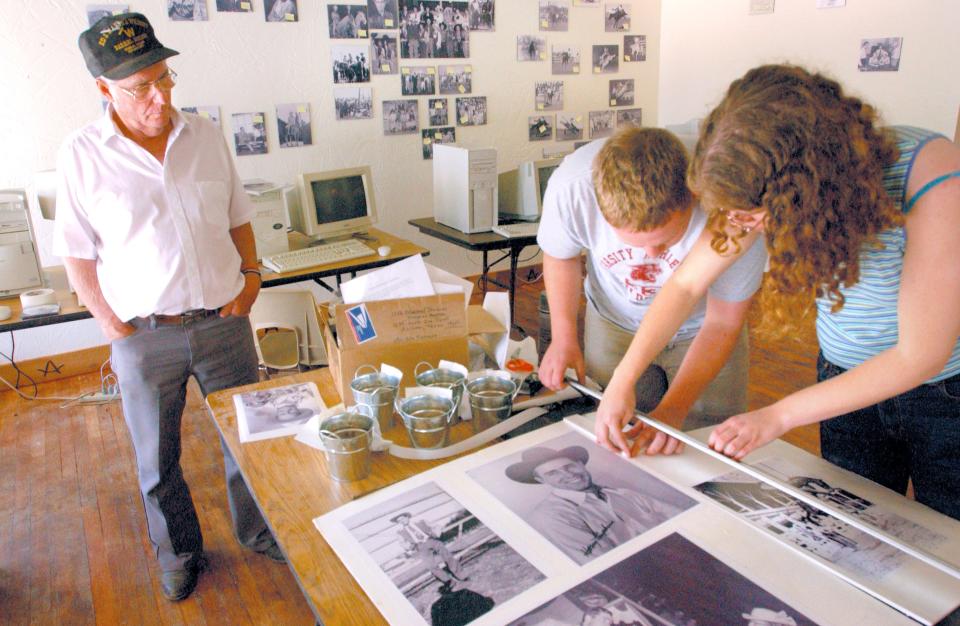 Champion bull rider Harry Tompkins watches as volunteers Katherine Duke and Keith Knight prepare photographs for display in Dublin's new Rodeo Heritage Museum in 2003. The picture next to their fingers is a photograph of Harry earlier in his career and many of the images in the museum are from his collection.