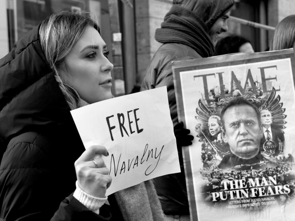 A protestor holds a sign reading "Free Navalny" and another poster shows the Time Magazine cover featuring Alexei Navalny.