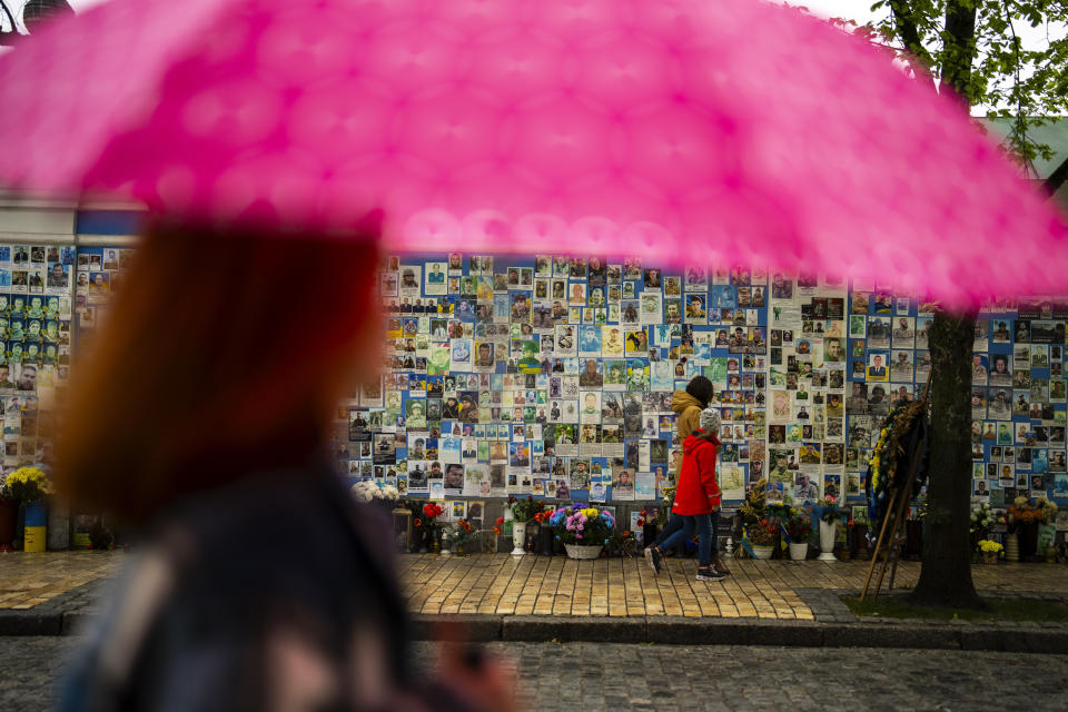 People walk past a memorial wall with photographs of Ukrainian soldiers killed during the war, at Saint Michael cathedral during a rainy morning in Kiev, Ukraine, Sunday, April 21, 2024. The House swiftly approved $95 billion in foreign aid for Ukraine, Israel and other U.S. allies in a rare Saturday session as Democrats and Republicans banded together after months of hard-right resistance over renewed American support for repelling Russia's invasion. (AP Photo/Francisco Seco)