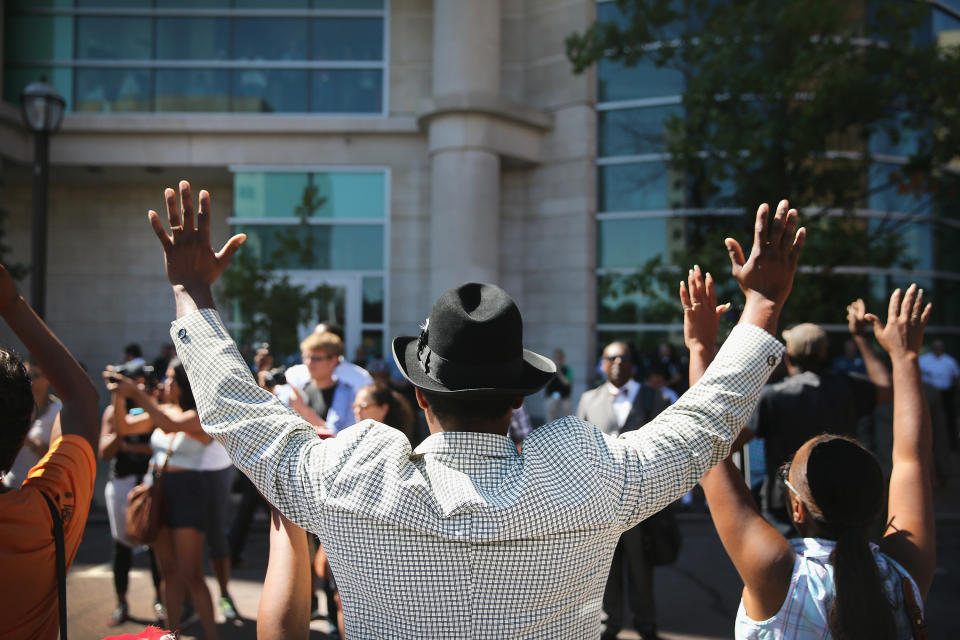 CLAYTON, MO - AUGUST 12:  Demonstrators raise their hands and chant 'hands up, don't shoot' during a protest over the killing of Michael Brown on August 12, 2014 in Clayton, Missouri. Some reports state that Brown hand his hands in the air when he was shot and killed by a police officer on Saturday in suburban Ferguson, Missouri. Two days of unrest including rioting and looting have followed the shooting in Ferguson.  Browns parents have publicly asked for order.  (Photo by Scott Olson/Getty Images)