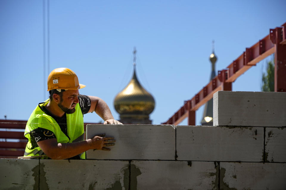 FILE - A construction worker works on the site of the new municipal medical center in Mariupol with an Orthodox church in the background, in territory under control of the government of the Donetsk People's Republic, in eastern Ukraine, Wednesday, July 13, 2022. This photo was taken during a trip organized by the Russian Ministry of Defense. (AP Photo/File)