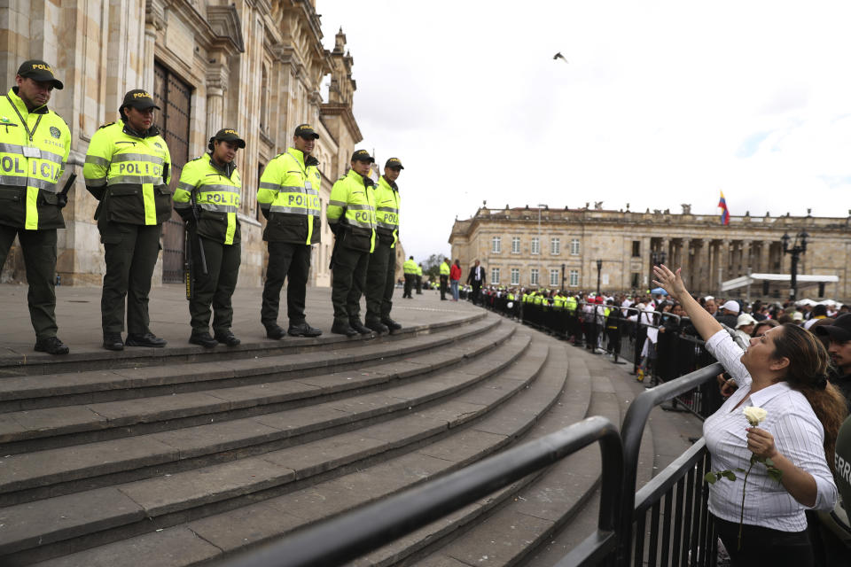 Una mujer saluda a policías que vigilan la Catedral el domingo 20 de enero de 2019 antes de una misa en honor de quienes perdieron la vida por el estallido de un coche bomba en una academia policial en Bogotá, Colombia. (AP Foto/Ricardo Mazalan)