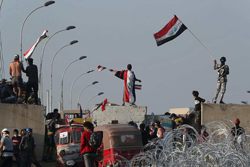 Iraqi anti-government protesters take control of the concrete walls and barriers set by security forces close the Al-Sanak Bridge leading to the Green Zone during a demonstration in Baghdad, Iraq, Thursday, Oct. 31, 2019. Late Wednesday, hundreds of people headed to the Al-Sanak Bridge that runs parallel to the Joumhouriya Bridge, opening a new front in their attempts to cross the Tigris River to the Green Zone. Security forces fired volleys of tear gas that billowed smoke and covered the night sky. (AP Photo/Hadi Mizban)